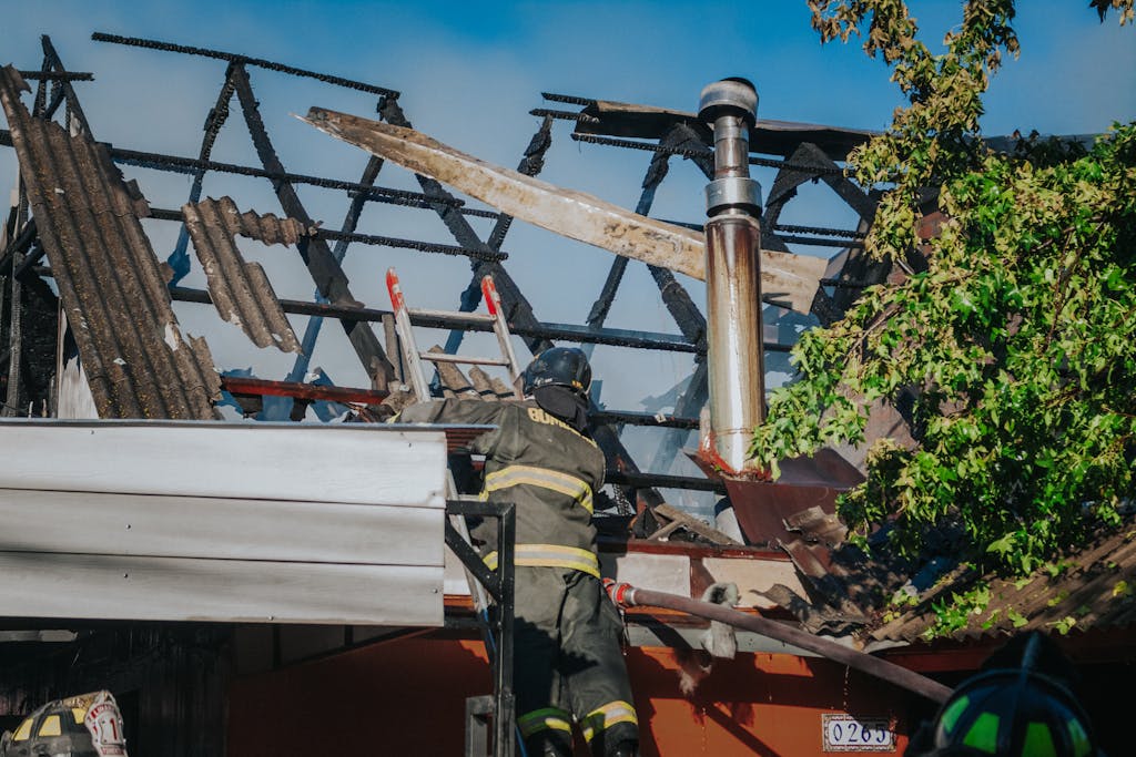 A firefighter tackles the aftermath of a house fire, clearing debris from a burned roof.