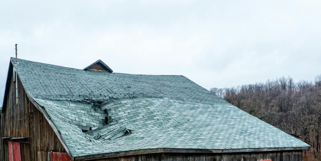 A weathered wooden barn with a damaged roof in a rural New York landscape.