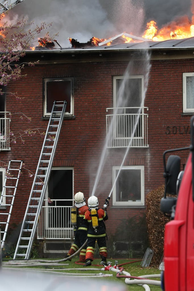 Firefighters extinguishing a fire in a residential building with ladders and hoses.