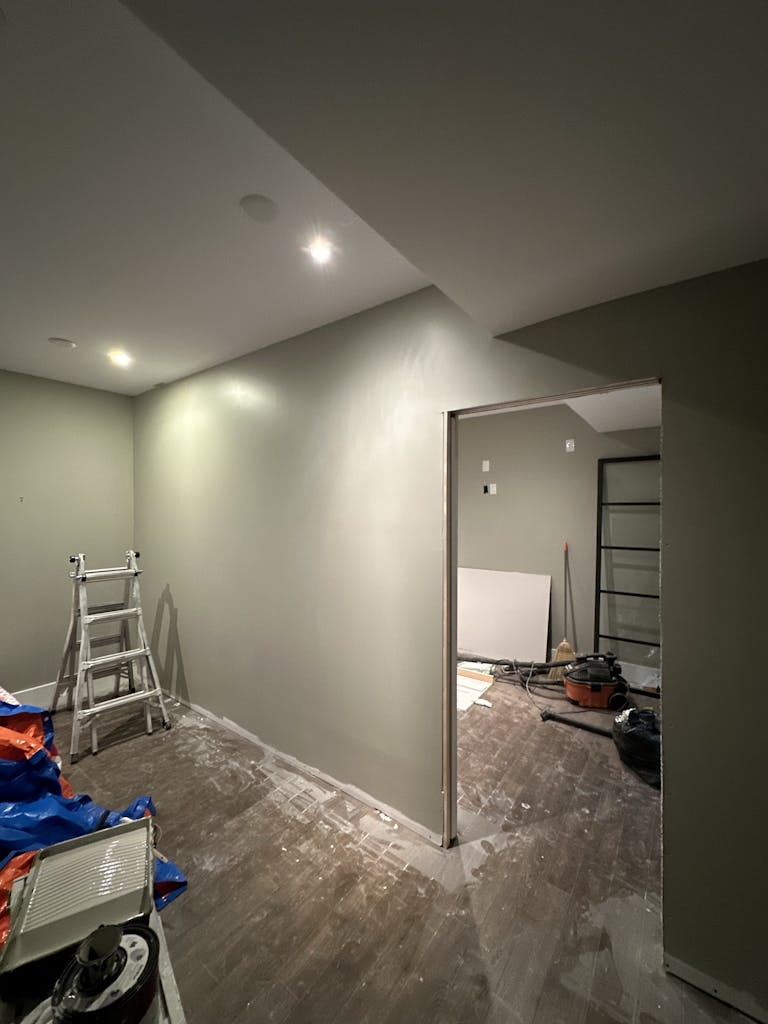 Interior view of a room under renovation, featuring a ladder and tools on the wooden floor.