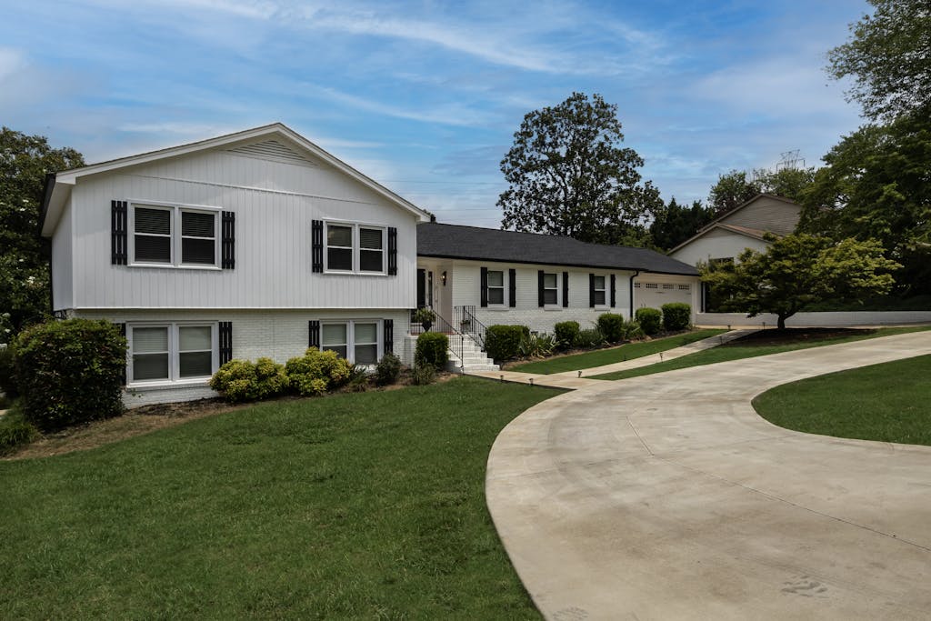 Modern suburban home with a large driveway and lush green lawn under a clear blue sky.